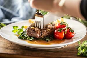 pessoa cortes para dentro uma cozinhou bife com garfo e faca com legumes em uma lado foto