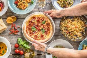pizza salame dentro cozinhar mãos. chefe de cozinha servindo pizza diavolo dentro a meio mesa cheio do italiano refeições foto
