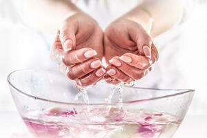 detalhe do mão com perfeito manicure elevado a partir de uma vidro tigela cheio do água com flor pétalas foto