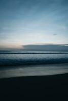 surpreendente tarde pôr do sol Sombrio azul céu em a indiano oceano com ondas em bali ilha. tropical verão fundo foto