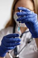 uma médica usando uma máscara médica coloca a vacina contra o coronavírus em uma seringa