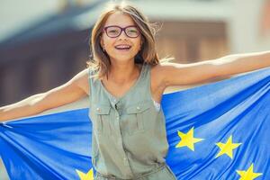 eu bandeira. fofa feliz menina com a bandeira do a europeu União. jovem Adolescência menina acenando com a europeu União bandeira dentro a cidade foto