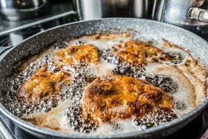 Schnitzels ser frito dentro óleo dentro uma Sombrio panela foto