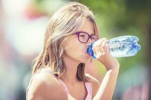 jovem menina bebendo fresco água em uma quente verão dia foto