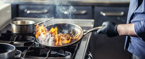 chefe de cozinha dentro a cozinha inclina-se panela para a lado para álcool dentro isto para pegar fogo para gás forno, iniciando para flambar a Comida foto