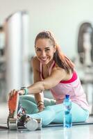 mulher alongar dela pernas e aquece acima antes tendo uma haltere exercite-se dentro a Academia com água garrafa pronto Próximo para dela foto