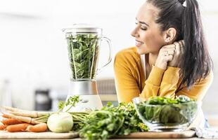 uma jovem mulher parece às uma liquidificador cheio do espinafre, fresco legumes por aí dela foto