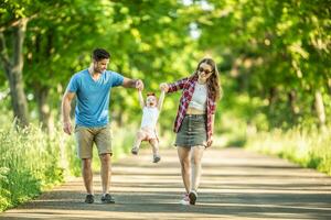 feliz família, pai e mãe desfrutando uma andar dentro a parque com seus pequeno filha foto