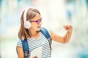 estudante com bolsa, mochila. retrato do moderno feliz adolescente escola menina com saco mochila fones de ouvido e tábua. menina com dental suspensórios e óculos. foto