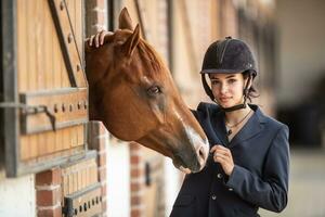 fêmea jóquei dentro capacete e equitação uniforme pega pronto para cavalo raças em pé Próximo para Está pintura cavalo foto