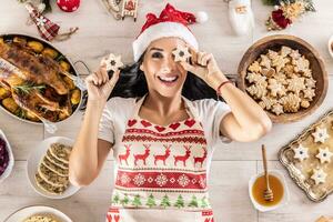 uma alegre cozinhar dentro uma Natal avental mentiras em a terra e cobre dela olhos com bolos, cercado de tradicional feriado pratos e bolos foto