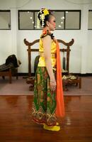 uma tradicional indonésio dançarino em pé dentro uma amarelo traje e a laranja cachecol suspensão baixa dela corpo foto