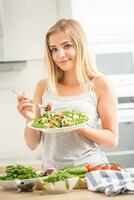 jovem feliz Loiras menina comendo saudável salada a partir de Rúcula espinafre tomates azeitonas cebola e Oliva óleo foto