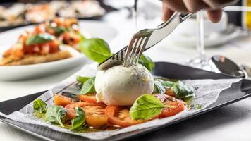 talheres usava para cortar para dentro uma bola do mozzarella di búfala em uma caprese estilo salada foto