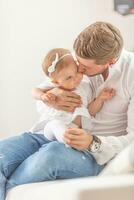 jovem pai segurando e se beijando dele bebê criança pequena menina em dela bochecha às casa foto