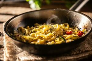 vegetariano tagliatelle com abobrinha e tomates servido dentro chiando quente panela foto