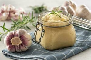 aromático alho colar dentro uma vidro jarra liderar em rústico cozinha pano com lâmpadas e descascado cravo e alecrim foto