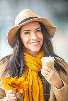 lindo jovem senhora dentro chapéu com outono folhas e café Leve embora caneca dentro dela mãos foto