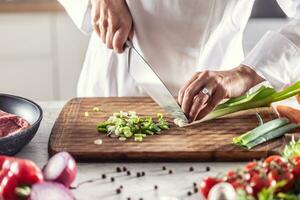 chefe de cozinha finamente costeletas Primavera cebola em uma de madeira corte borda foto