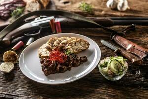 porcelana prato cheio do veado carne de veado Goulash ensopado servido com bolinho de massa e fresco salada Como a Aperitivo. Comida é cercado de Caçando acessórios tal Como Caçando espingarda, balas e rústico faca foto