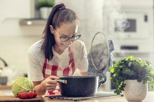 dona de casa dentro avental abre tampa do uma Panela olhando para dentro isto enquanto cozinhando dentro a cozinha às casa foto