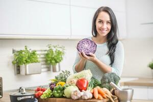 alegre jovem mulher com vermelho repolho e fresco legumes dentro dela cozinha preparando uma saudável almoço foto