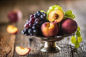 maduro uvas e pêssegos dentro rústico tigela e de madeira mesa foto