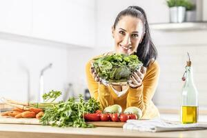 sorridente mulher com uma tigela cheio do espinafre folhas ao longo com fresco legumes e Oliva óleo dentro dela cozinha foto