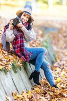 sorridente boa aparência fêmea fotógrafo dentro uma chapéu e à moda outono roupas leva As fotos lado de fora em uma ensolarado outono dia