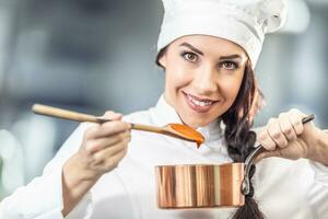 profissional fêmea chefe de cozinha detém uma de madeira colher com laranja molho e uma panela vestindo chapéu e chef uniforme foto