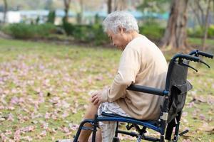 paciente asiático sênior ou idosa senhora idosa dor no joelho na cadeira de rodas no parque, conceito médico forte e saudável. foto