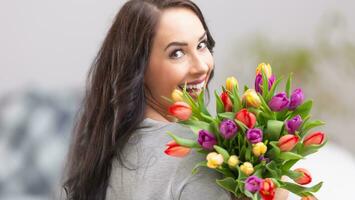 feliz Sombrio cabelos mulher segurando uma adorável ramalhete cheio do tulipas durante nacional mulheres dia foto