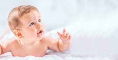 retrato do fofa criança pequena Garoto deitado em cama. recém-nascido criança dentro quarto. bebê mentiras em dele barriga e levanta a cabeça foto