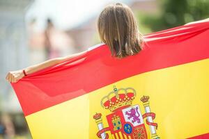 feliz menina turista caminhando dentro a rua com espanhol bandeira foto