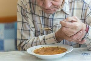 idosos homem com Parkinson doença detém colher dentro ambos mãos foto