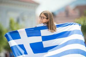 feliz menina turista caminhando dentro a rua com Grécia bandeira foto