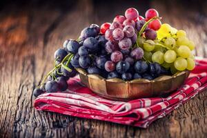 uva. grupo do multicolorido uvas dentro retro tigela em velho carvalho mesa foto