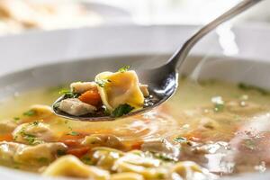 colher do tortellini, cenoura, e frango ocupado a partir de uma quente sopa dentro uma prato foto