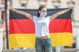 mulher vestindo uma face mascarar detém uma bandeira do Alemanha atrás dela foto