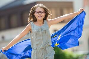 eu bandeira. fofa feliz menina com a bandeira do a europeu União. jovem Adolescência menina acenando com a europeu União bandeira dentro a cidade foto