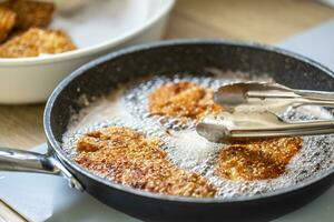 detalhe do panela com Schnitzels borbulhante dentro quente óleo e alicate levando eles Fora foto