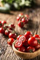 fresco cereja tomates dentro de madeira tigela em velho carvalho mesa foto