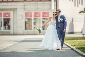 uma jovem somente casado casal caminhando alegremente dentro a Cidade dentro Casamento vestes com uma lindo ramalhete. noivo é se beijando dela noiva foto