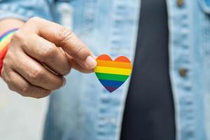 senhora asiática vestindo jaqueta jeans azul ou camisa jeans e segurando o coração da bandeira da cor do arco-íris, símbolo do mês do orgulho LGBT, comemorar anual em junho social de gays, lésbicas, bissexuais, transgêneros, direitos humanos. foto