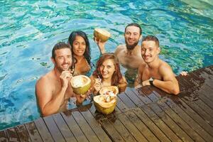 grupo do amigos desfrutando coco bebidas dentro a piscina foto