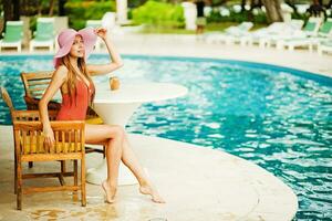 uma mulher dentro uma Rosa chapéu sentado às uma mesa perto uma piscina foto