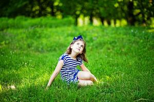 uma pequeno menina sentado em a Relva dentro uma campo foto