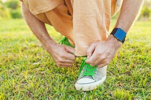 uma homem amarrar dele sapatos em uma gramíneo campo foto