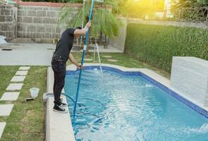 homem limpeza e mantendo natação piscinas com uma sucção mangueira. jovem homem limpeza uma natação piscina com uma vácuo mangueira, manutenção pessoa limpeza piscina com vácuo mangueira foto