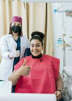 dentista com paciente sorridente e dando polegar acima. fêmea dentista com satisfeito paciente sorridente às Câmera e dando polegar acima, retrato do fêmea dentista com paciente sorridente às Câmera dentro escritório foto